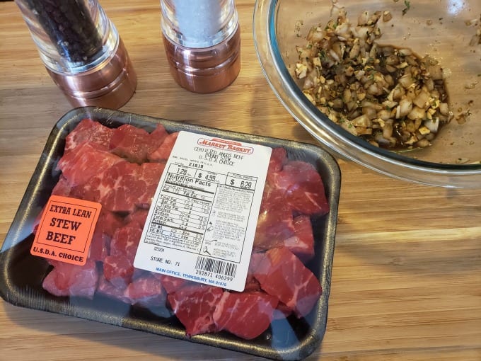 Package of Certified Angus Beef extra lean beef tips on a cutting board next to salt and pepper grinders and a bowl of marinade.