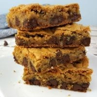 A stack of chocolate chip cookie bars on a white plate with a blue towel in the background.