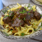 Close up image of beef tips with gravy over noodles.