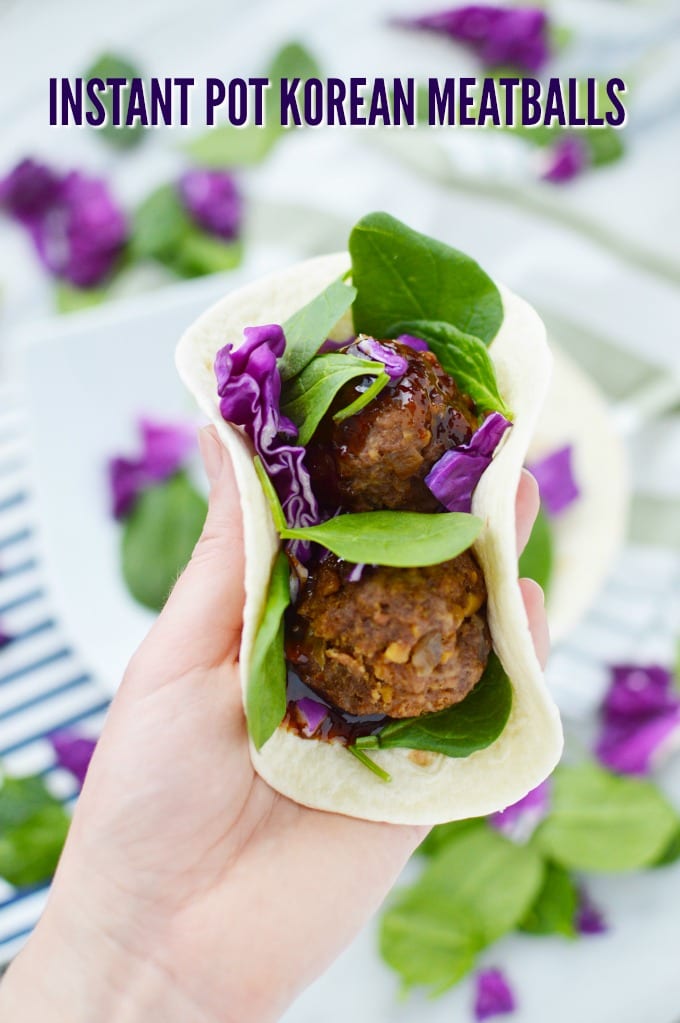 A hand holds a soft flour tortilla stuffed with spinach, Korean Meatballs and purple cabbage. 