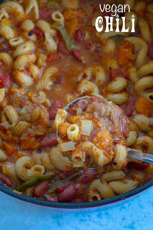 A serving spoon filled with vegan chili hovering over a Dutch oven filled with vegan chili
