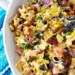 A close up of a large white bowl full of ornbread Salad., nex to a multi-hued blue striped towel.
