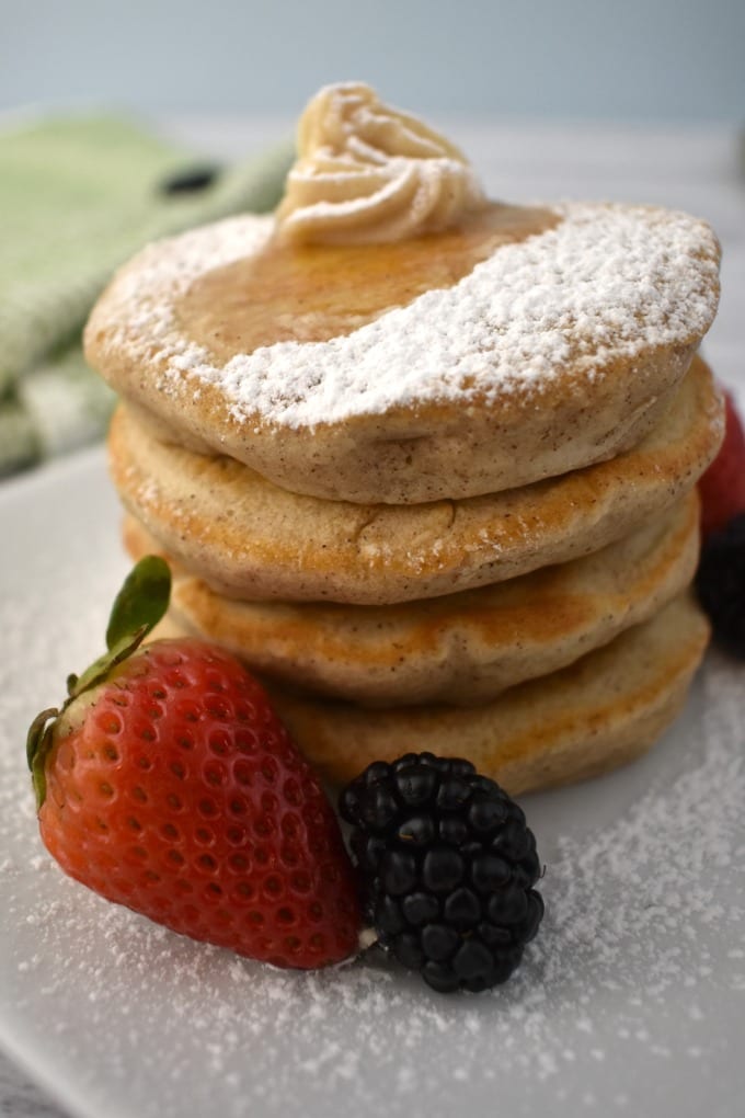 Stack of Silver Dollar Pancakes on a white plate with a dollop of butter and drizzle of maple syrup, garnished with fresh strawberries and black berries