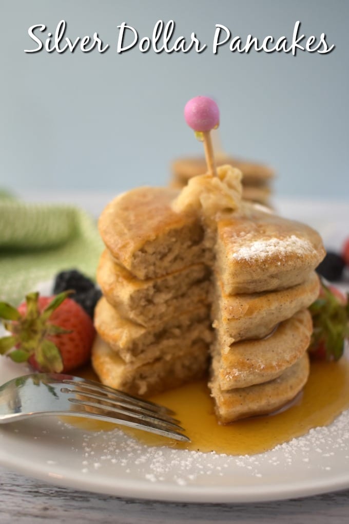 Stack of Silver Dollar Pancakes on a white plate with a dollop of butter and drizzle of maple syrup, garnished with fresh strawberries and black berries