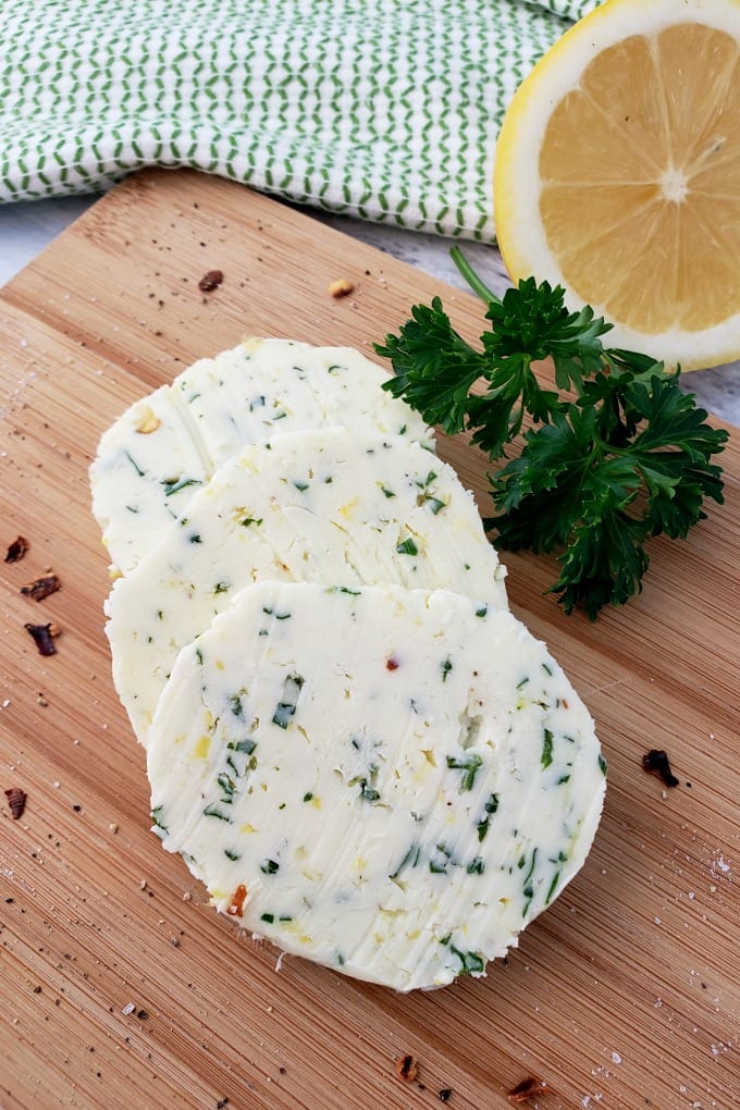 Round slices of Cowboy Butter on a cutting board with a sprig of parsley and a halved lemon.