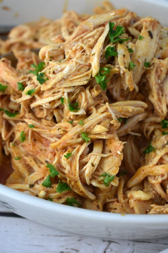 Tender spicy slow cooker buffalo chicken piled in a large white bowl, sprinkled with chopped parsley.
