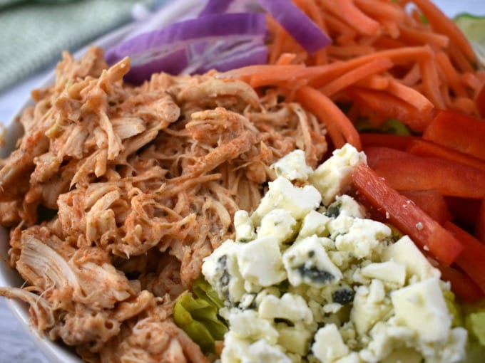 Buffalo chicken in a bowl with veggies and cheese.