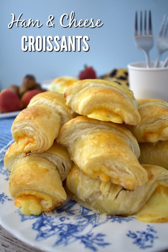 Ham and Cheese Croissants sit on a blue and white plate with forks and strawberries in the background
