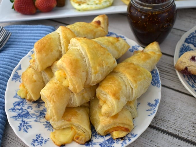 Ham and Cheese Croissants piled on a blue and white plate next to a jar of fig jam.