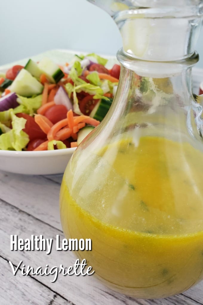 A cruet of golden lemon Vinaigrette in the foreground with a garden salad in the background.