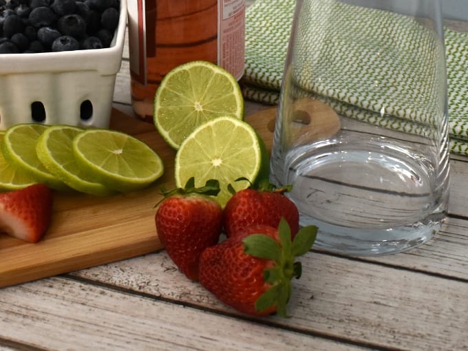 Strawberries and lime on cutting board with pitcher.
