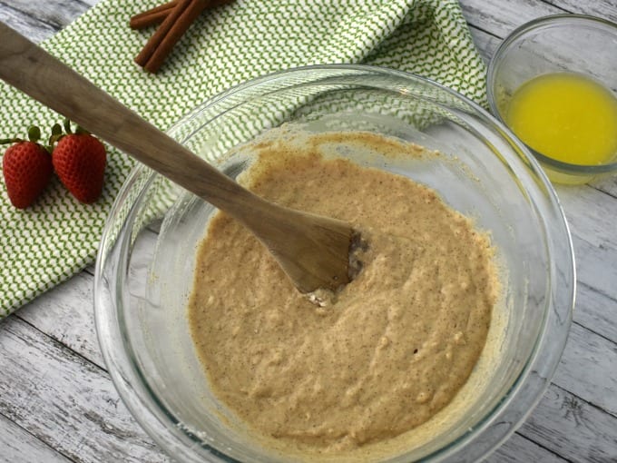 Silver Dollar Pancake Batter in a clear bowl with a wooden spoon. A small ramekin of melted butter nearby.