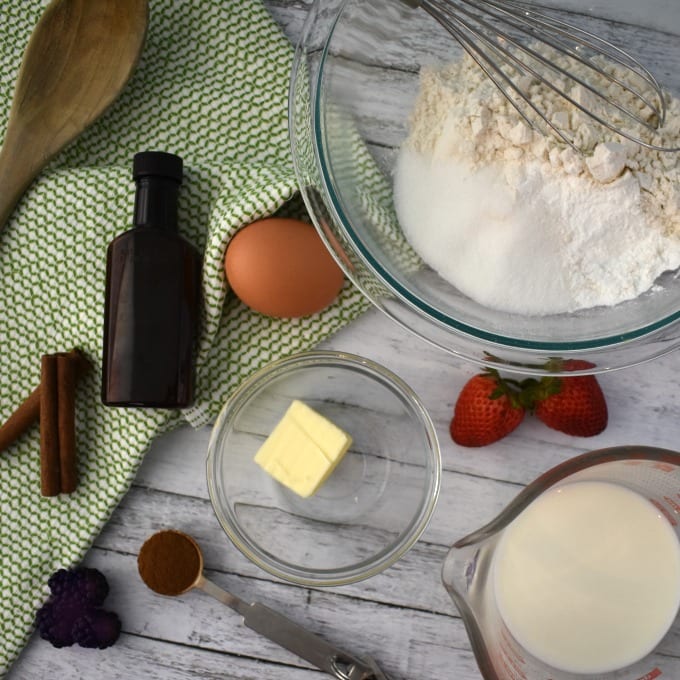 Silver Dollar Pancake Ingredients including butter in a small ramekin, milk in a measuring cup, glass bowl with flour and sugar, a whole egg, a wooden spoon.