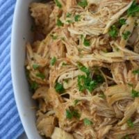 Tender spicy slow cooker buffalo chicken piled in a large white bowl, sprinkled with chopped parsley.
