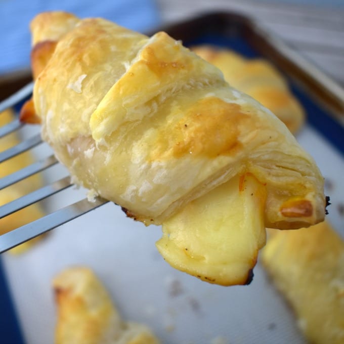 A silver spatula holds a ham and cheese croissant up.