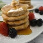 Stack of Silver Dollar Pancakes on a white plate with a little butter and drizzle of maple syrup, garnished with fresh strawberries and black berries