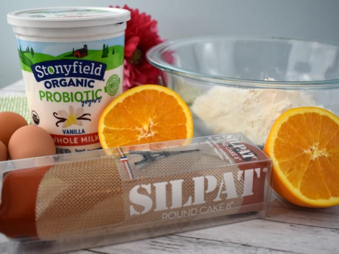 Yogurt Cake Ingredients such as Stonyfield Yogurt, eggs, halved oranges and a bowl with flour are pictured with a Silpat mat.