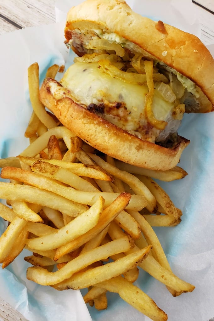A large butter burger with cheese on an onion roll with shoe string fries in a parchment paper lined basket.