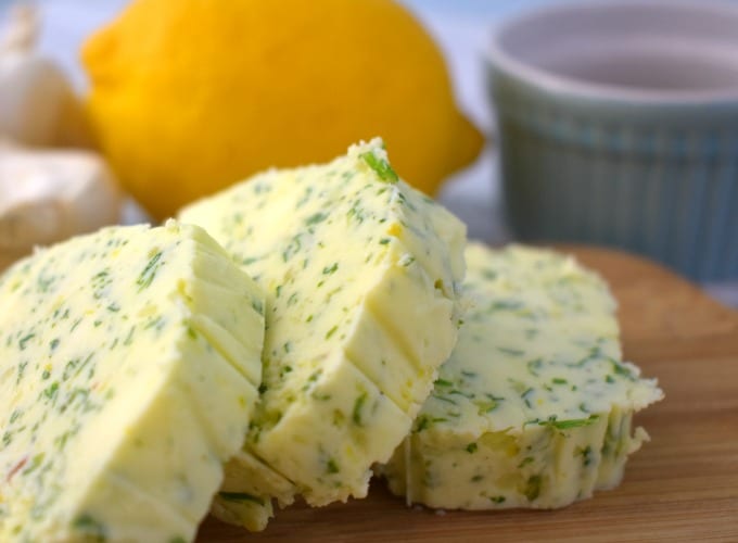 Sliced compound butter on a cutting board with a lemon, garlic and small ramekin in the background.