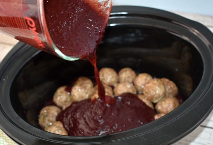 A Jelly and BBQ sauce  mixture is poured from a liquid measuring cup into a slow cooker.