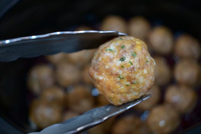 A set of tongs holds a single Meatball without the sauce.