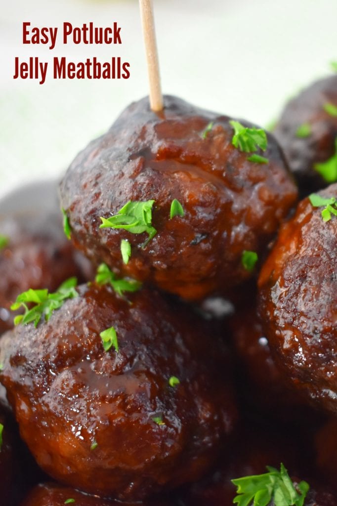 A close up of Crockpot Jelly Meatballs garnished with fresh chopped parsley. One meatball has a toothpick in it.