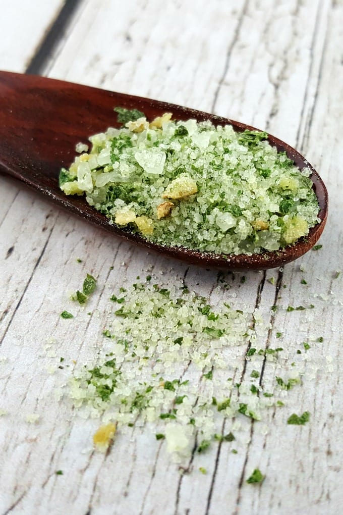 A close up of a spoonful of basil salt on a white wooden table.