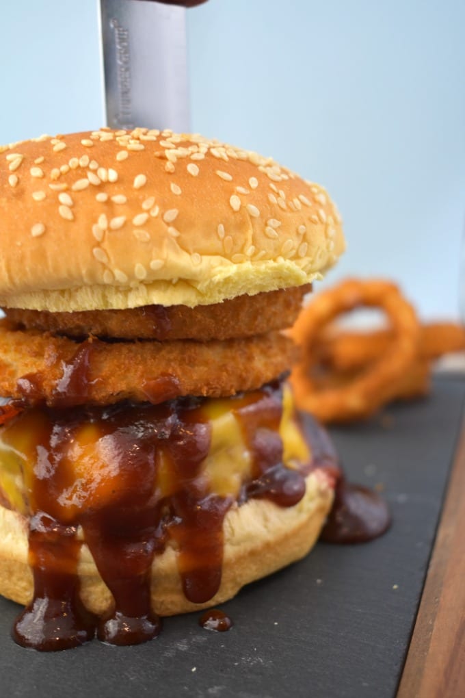 Incredible Cowboy Burger piled high with bacon and crispy onion rings on a sesame seed bun on a slate and wood cutting board