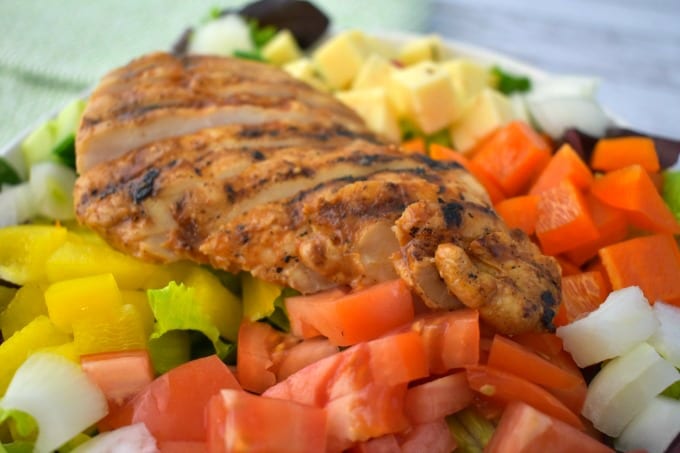 Spicy grilled chicken on top of a chopped salt with tomatoes, peppers, cucumbers, onions and pepper jack cheese cubes.