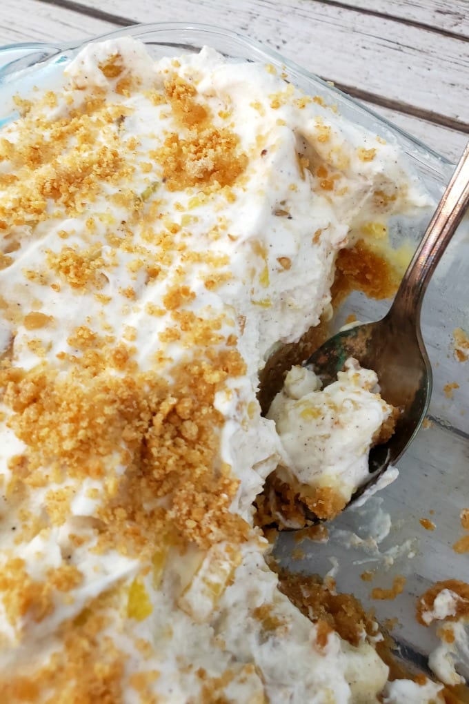 A close up of pineapple delight in a clear baking dish with a spoon on right right side.