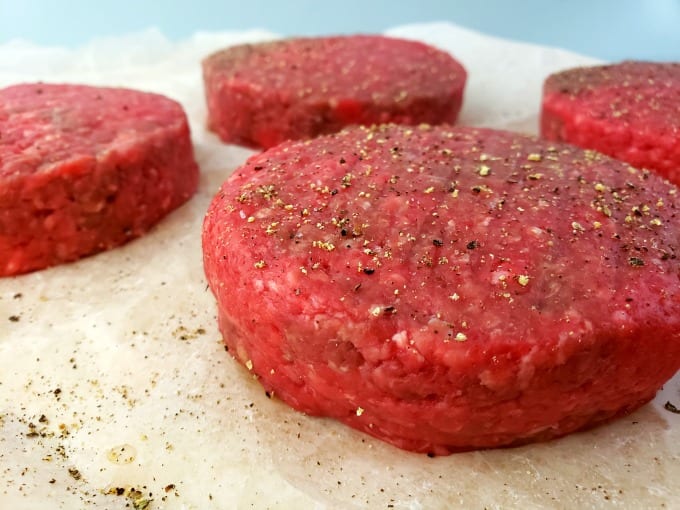Butter burger patties on parchment paper seasoned with salt and pepper.
