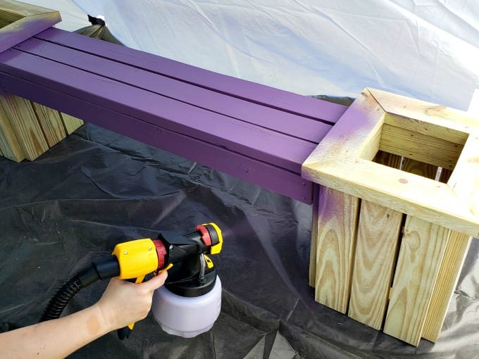 Woman painting a bench with a paint sprayer.