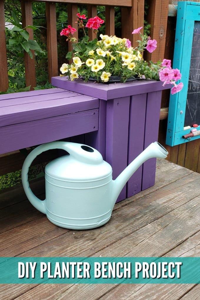 A watering can sits near the base of a purple Outdoor Planter Bench with pink and yellow flowers planted in it.