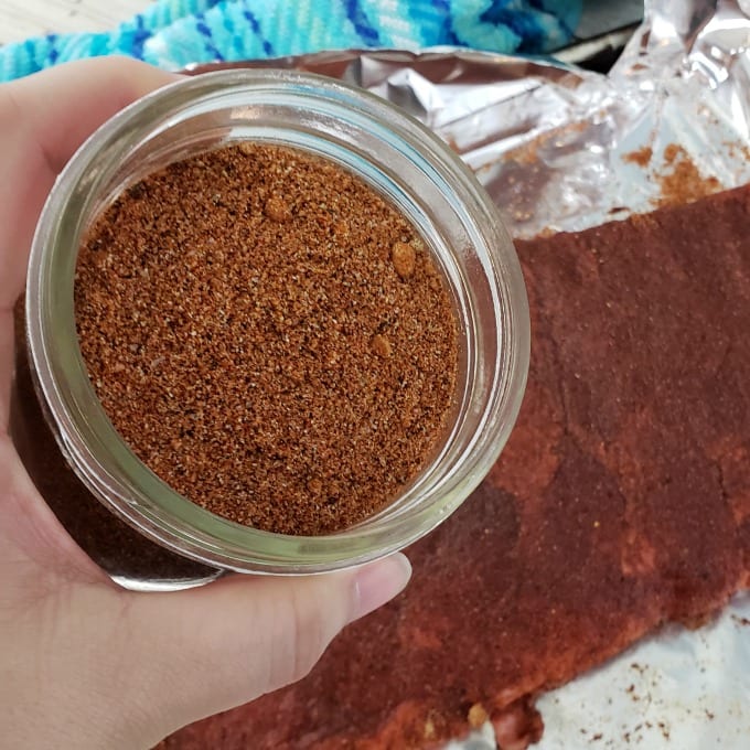 Close up image of a woman sprinkling the Best Pork Rub Seasoning on meat.