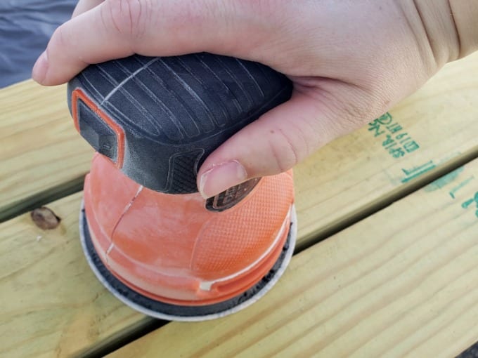 Hand holding an electric sander on top of wood.