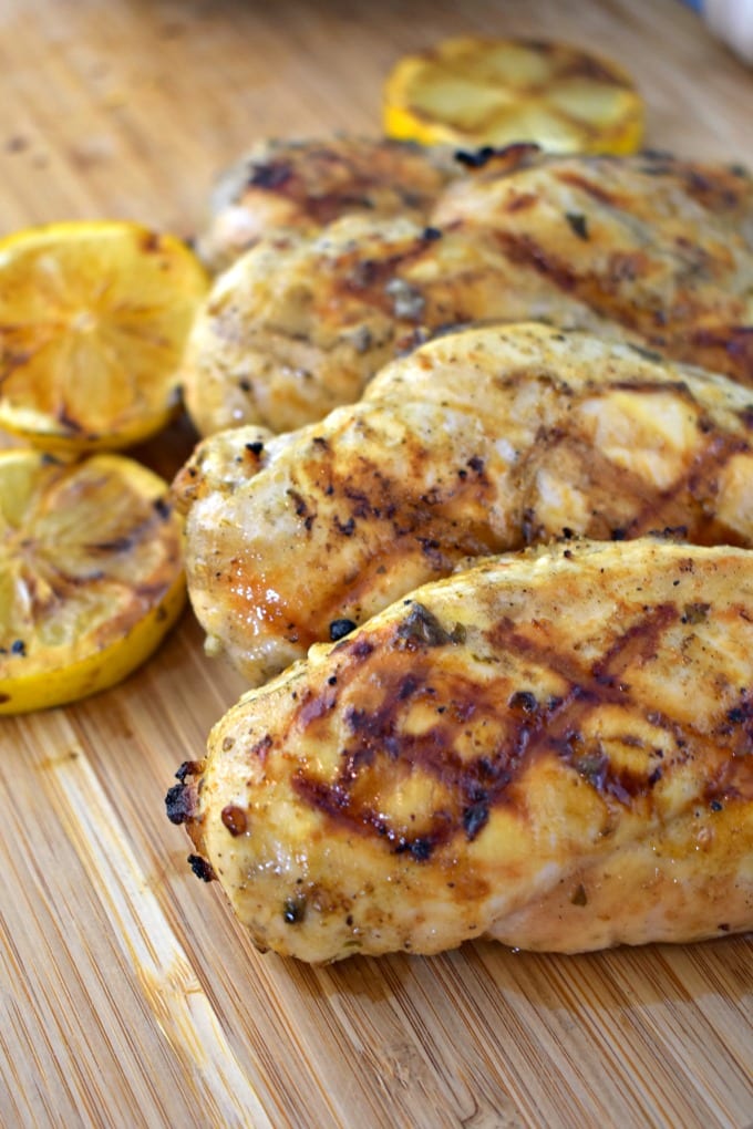 A close up of lemon garlic grilled chicken breasts on a cutting board with grilled lemon slices.