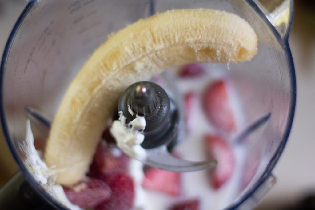 banana and strawberries in the pitcher of a blender