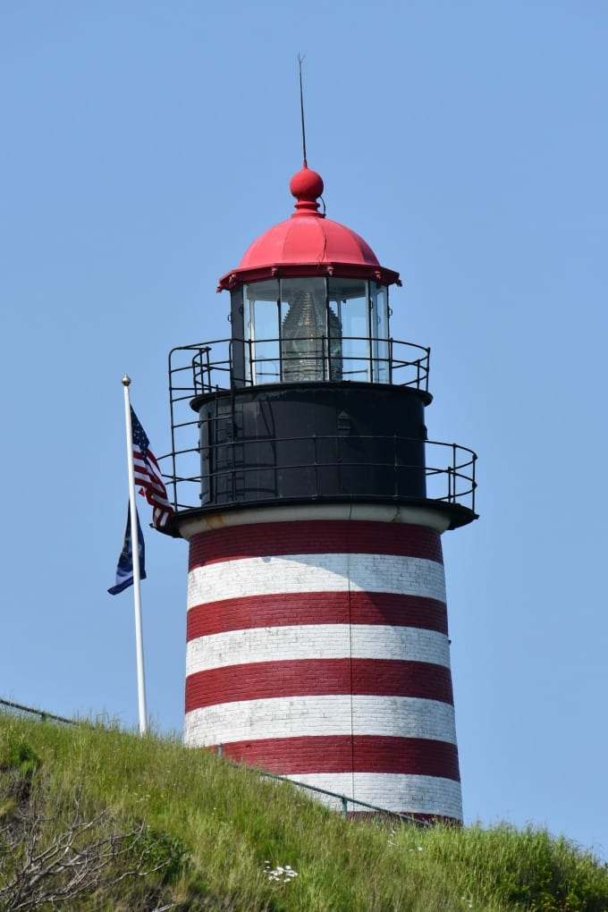 Image of West Quoddy Head Lighthouse next to an American flag and state of Maine flag blowing in the wind.