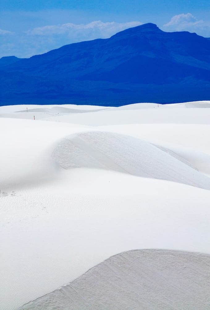 White sand dunes against a dark blue mountain at sunset.