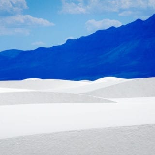White sand dunes against a dark blue mountain.