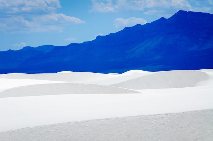 White sand dunes against a dark blue mountain.