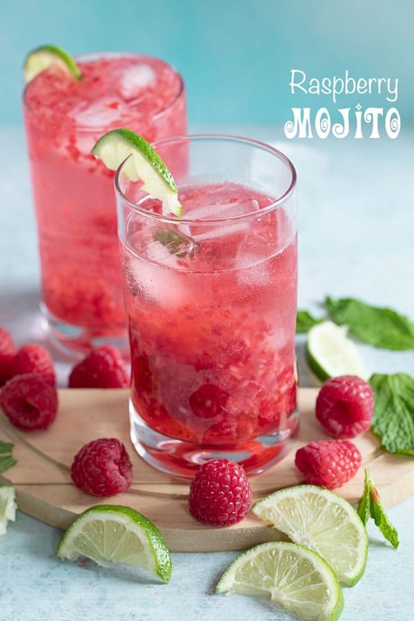 Front view of two glasses filled with raspberry mojito and surrounded by raspberries, lime and mint leaves