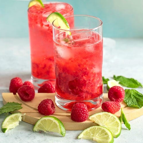 Raspberry mojito surrounded by fresh limes and raspberries