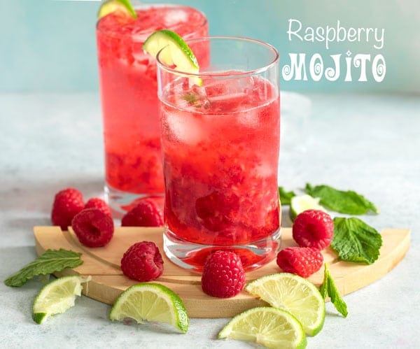 Front view of two glasses filled with raspberry mojito and surrounded by raspberries, lime and mint leaves