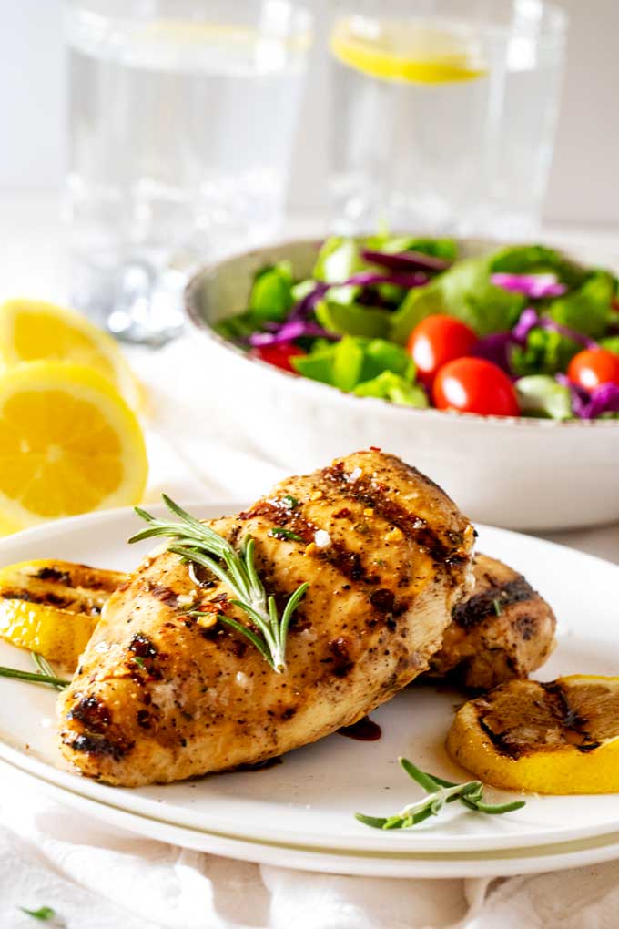 Side photo of Grilled Lemon Chicken on a white plate garnished with flakey salt and rosemary.