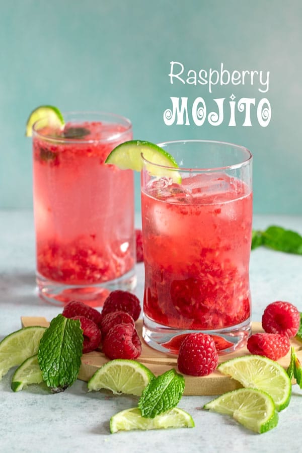 Front view of two glasses filled with raspberry mojito and surrounded by raspberries, lime and mint leaves