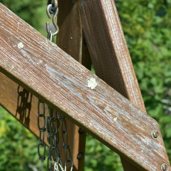 A close up of a shabby outdoor wooden swing.