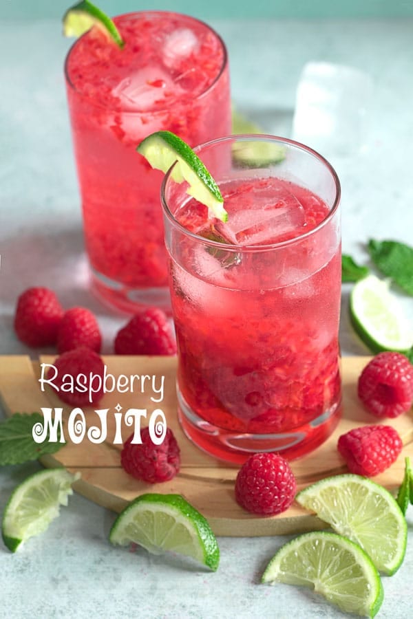Front view of two glasses filled with raspberry mojito and surrounded by raspberries, lime and mint leaves