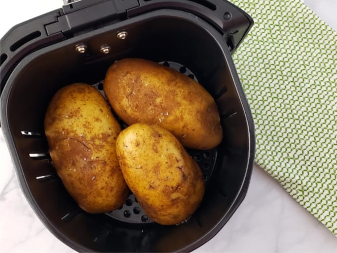 Three oil-rubbed russet potatoes in the basket of an air fryer.