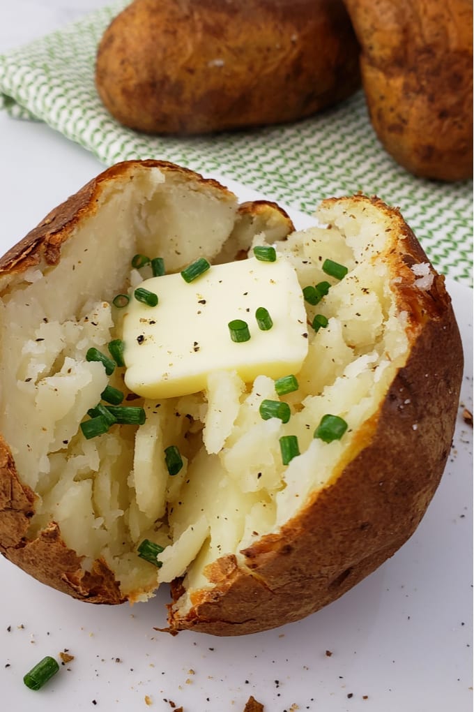 Baked potato on a white plate with a pat of butter and sprinkles with pepper and chopped chives.